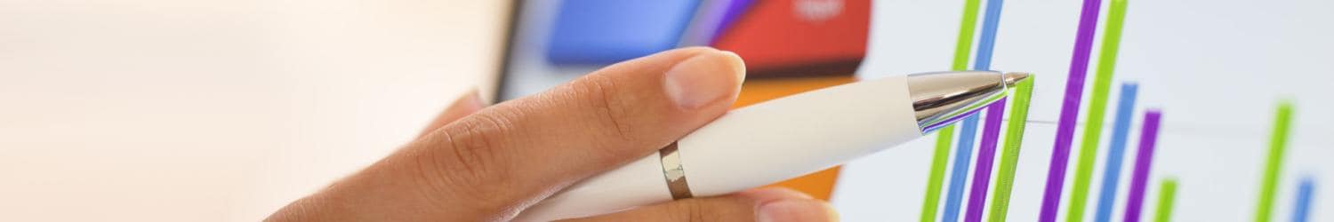 Nahaufnahme einer Hand, die einen Stift hält und auf ein buntes Balkendiagramm auf einem Bildschirm zeigt.