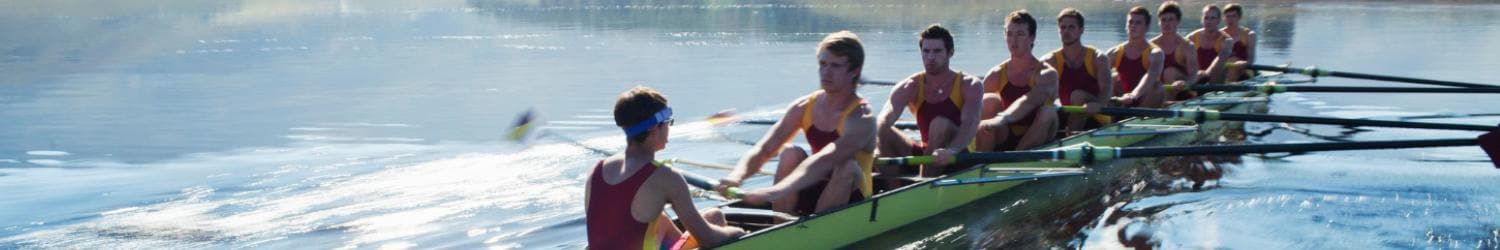 A team of eight rowers with a coxswain in matching uniforms steers a rowing boat across calm water.