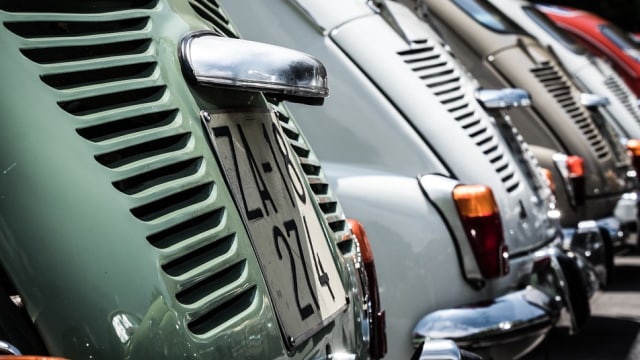 Eine Reihe eng geparkter Oldtimer. Die Rückansichten sind mit sichtbaren Nummernschildern und Rücklichtern zu sehen.