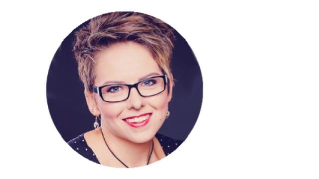 Person mit kurzen Haaren und Brille, die vor einem schwarzen Hintergrund lächelt.
