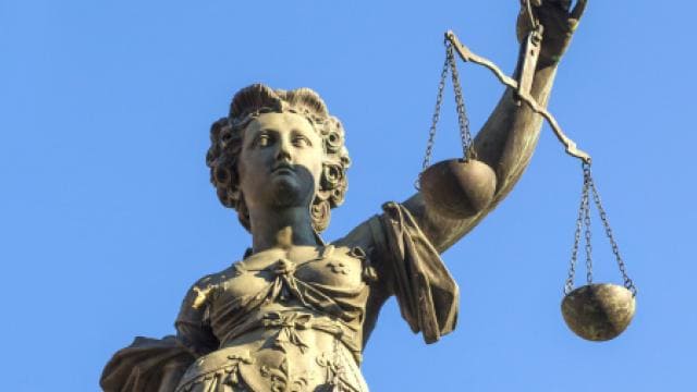 Eine Statue der Justitia, die vor einem klaren blauen Himmel eine Waage in der Hand hält und damit Fairness und Gerechtigkeit symbolisiert.