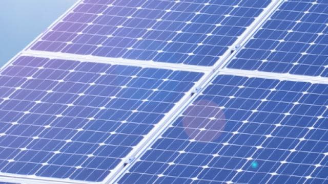 Nahaufnahme einer großen Anordnung blauer Solarmodule im Sonnenlicht.