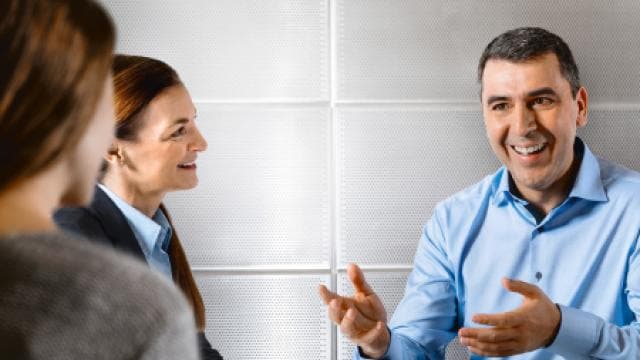 Menschen in einem professionellen Umfeld diskutieren, wobei ein Mann beim Sprechen gestikuliert und die anderen aufmerksam zuhören.